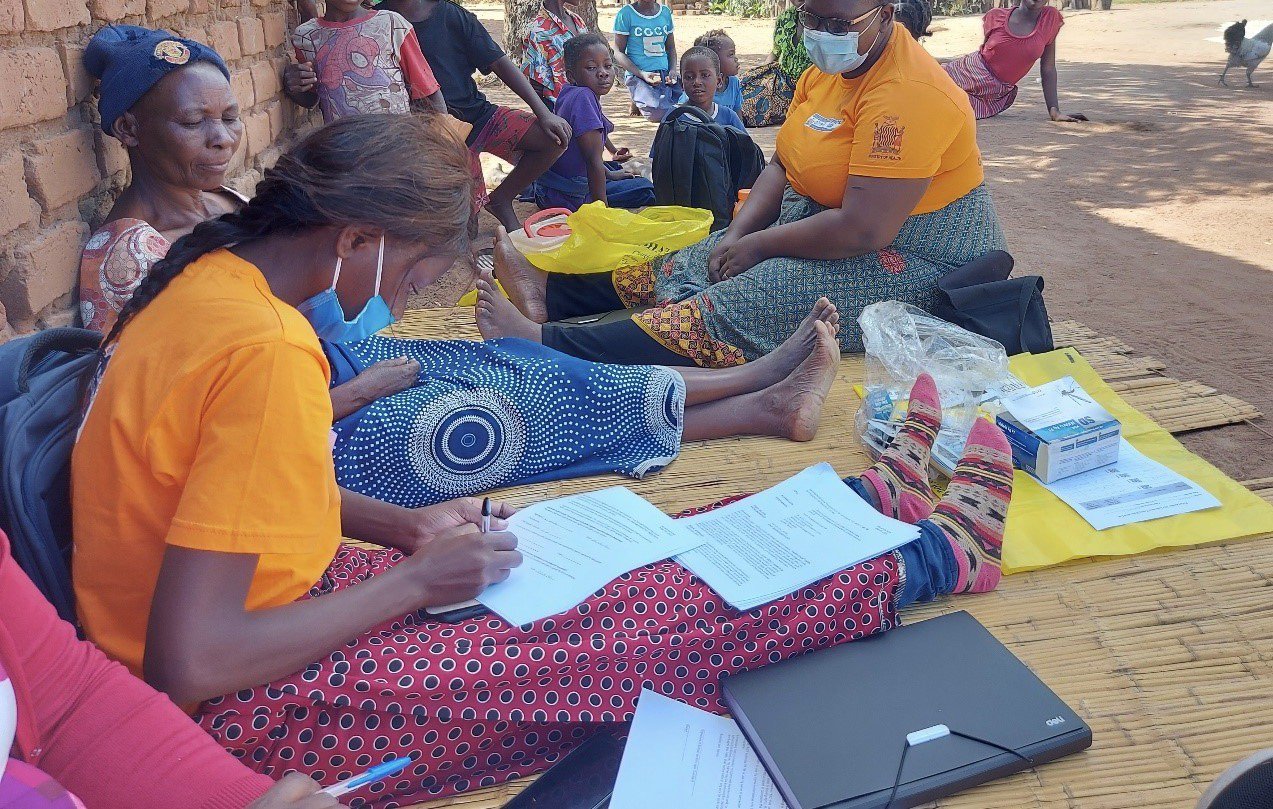 Community health workers Gertrude Banda (left in orange shirt) and Florid Mufwali (right in orange shirt) collect data during a baseline survey for the ProACT study in Chadiza District, Eastern Province, Zambia. Photo: PATH/Elizabeth Chiyende.