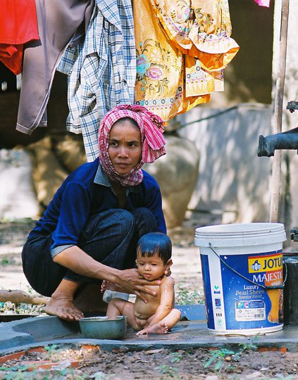 A woman washes an infant next to a water pump.