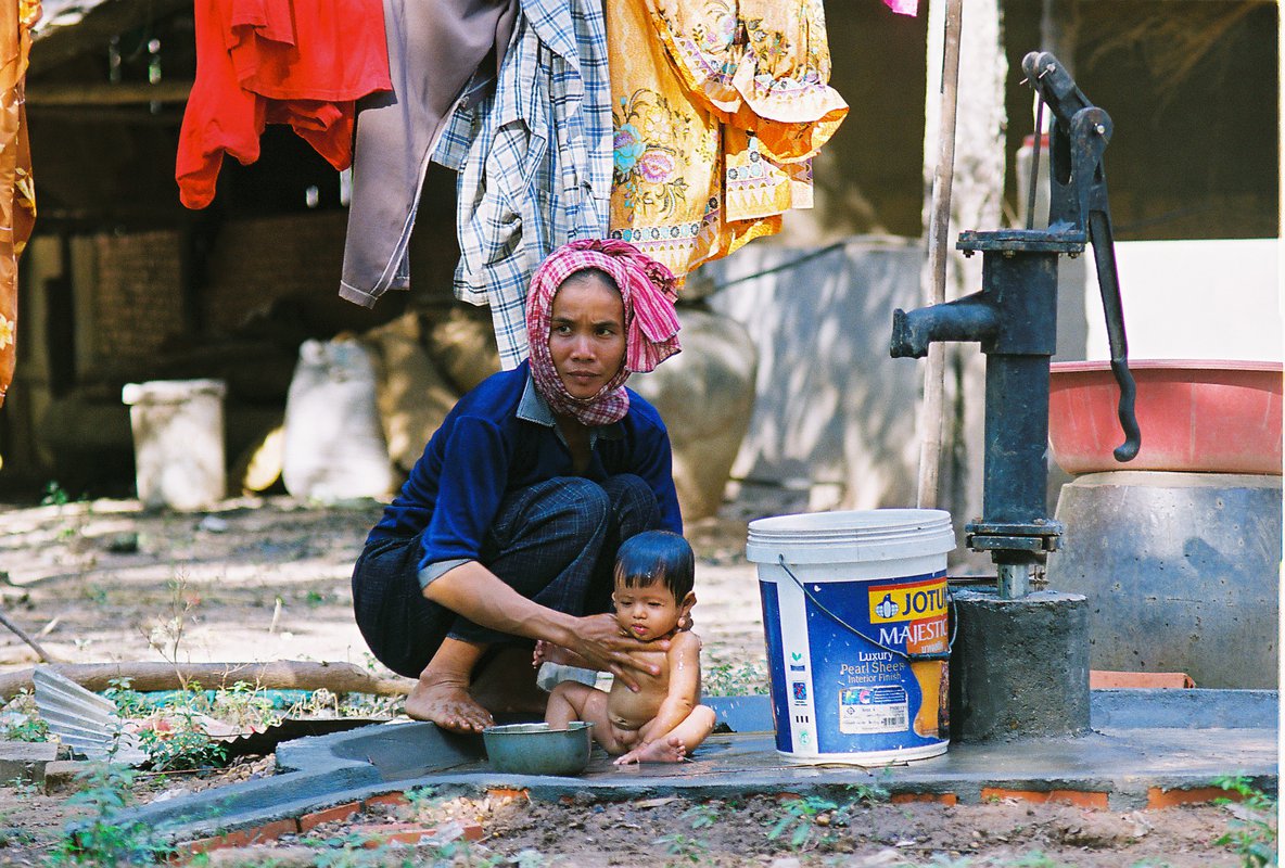 A woman washes an infant next to a water pump.