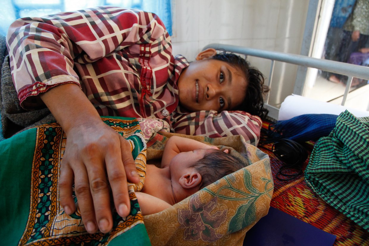 A woman lies on a bed with an infant.