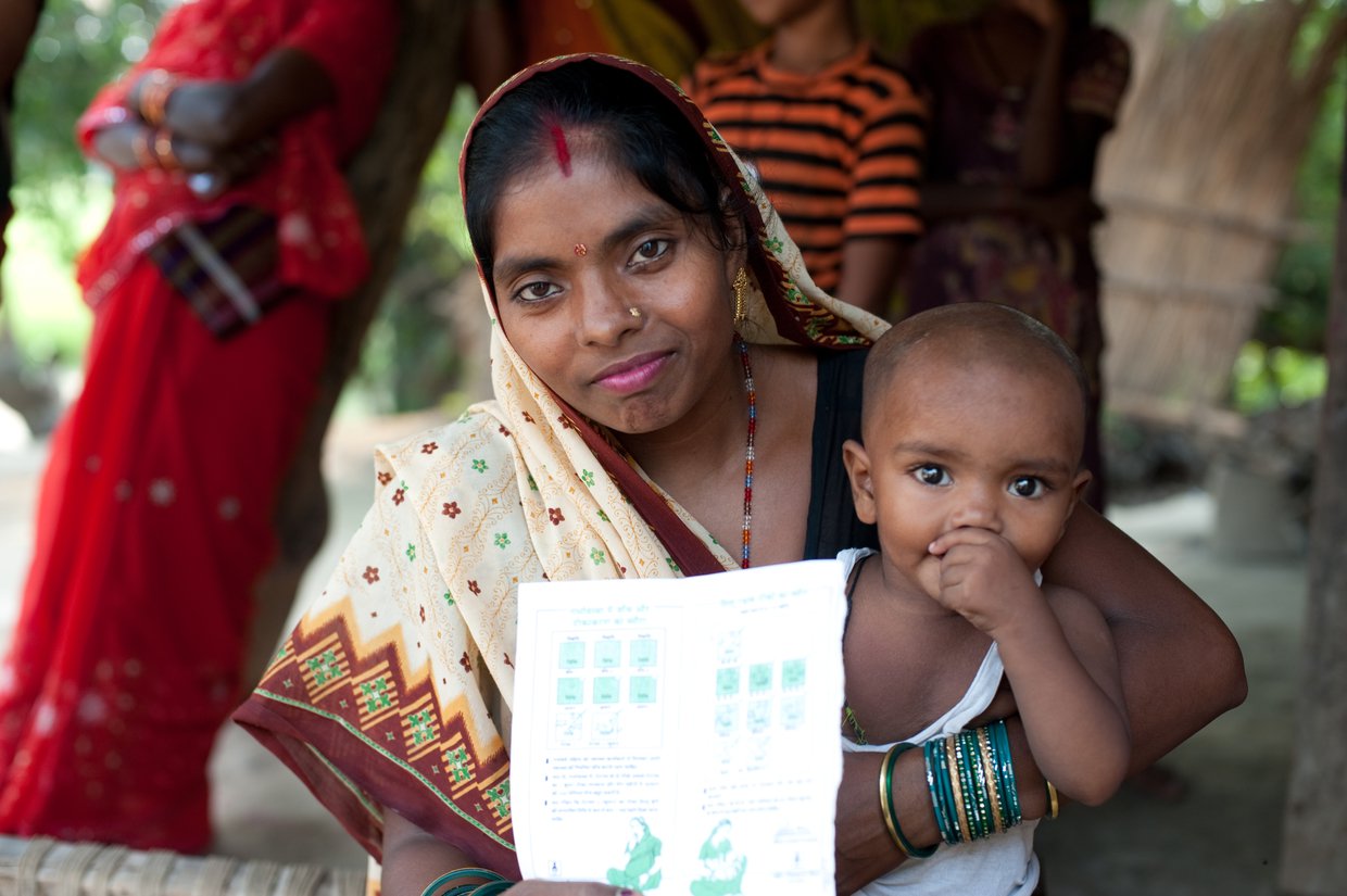A woman holds an immunizations record and her child.