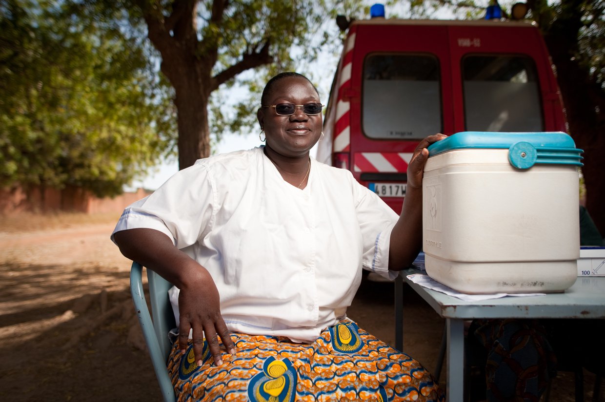 Female health worker sitting at a table, with a vaccine carrier.