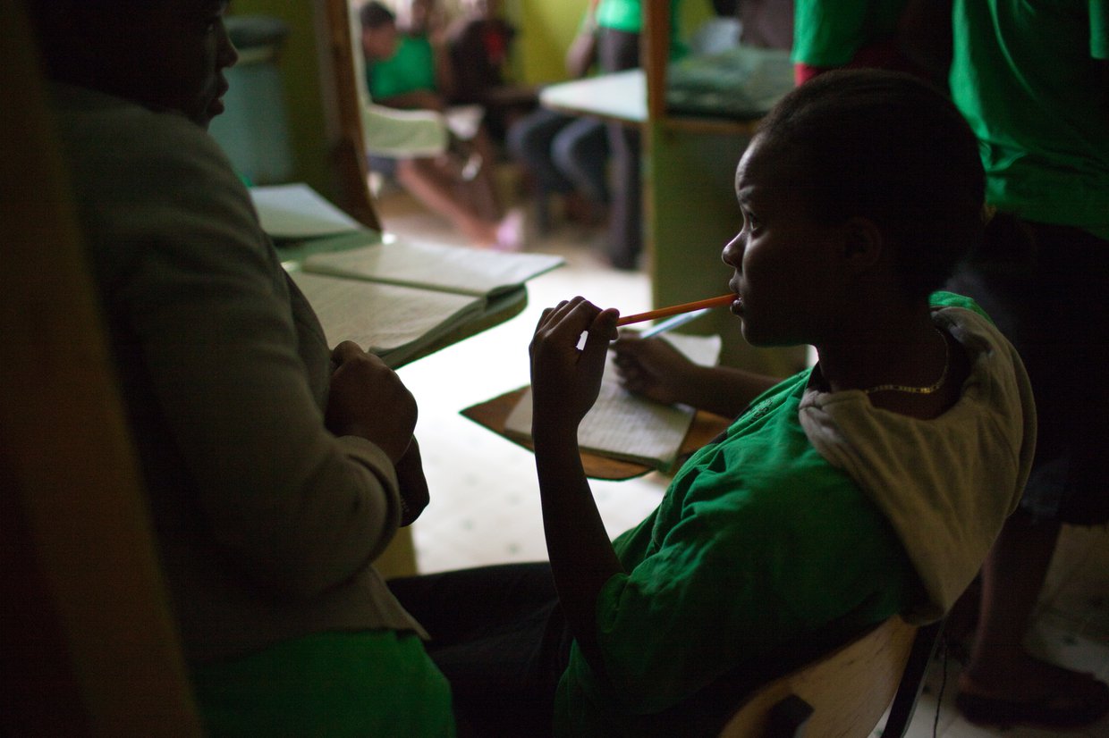 Adolescent female sitting at a table writing on a piece of paper. A woman is sitting at the table with her.