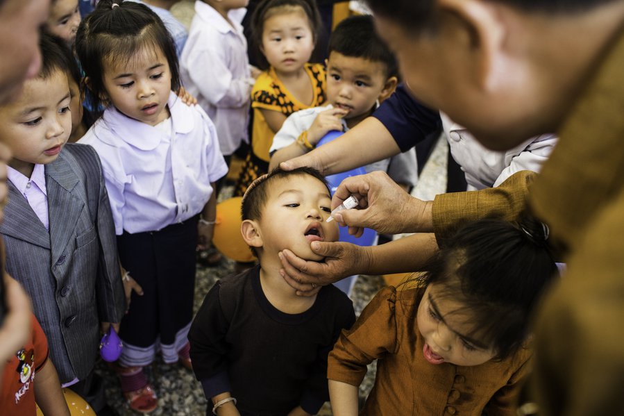 Child receives oral vaccine while others look on.