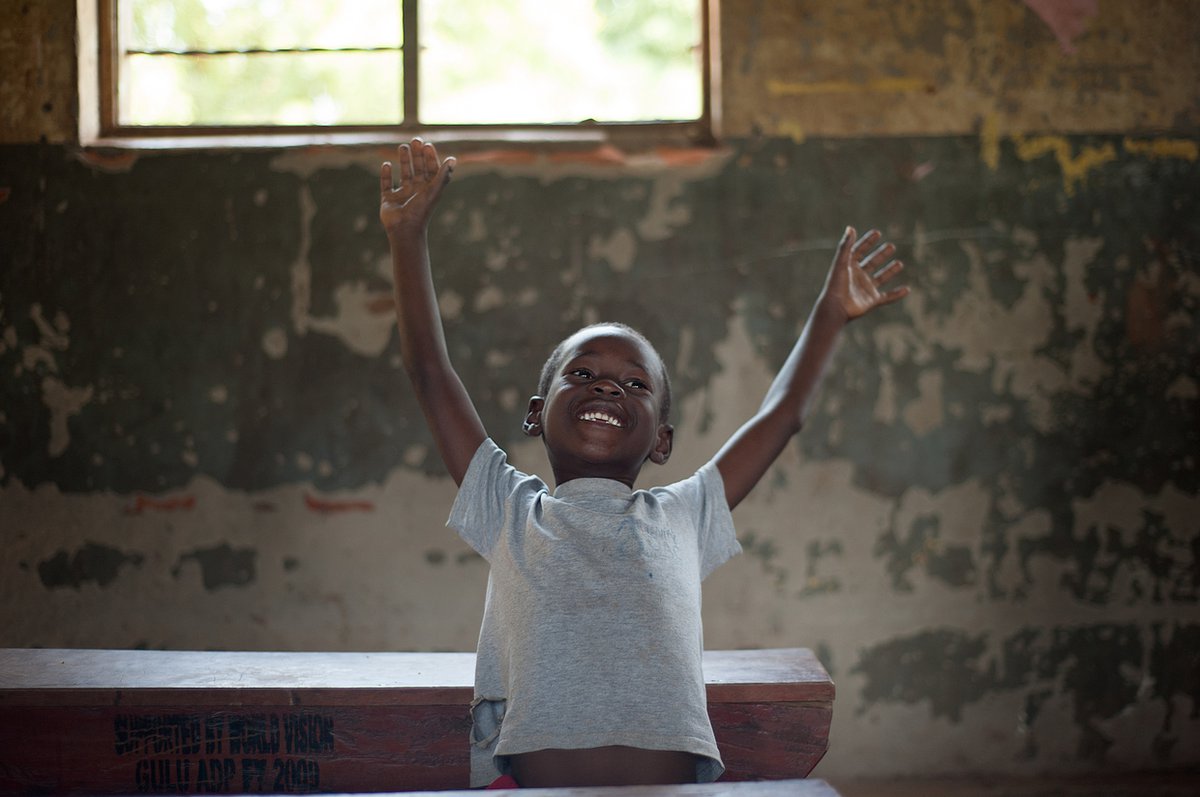 A little boy stands inside with his arms stretched upward.