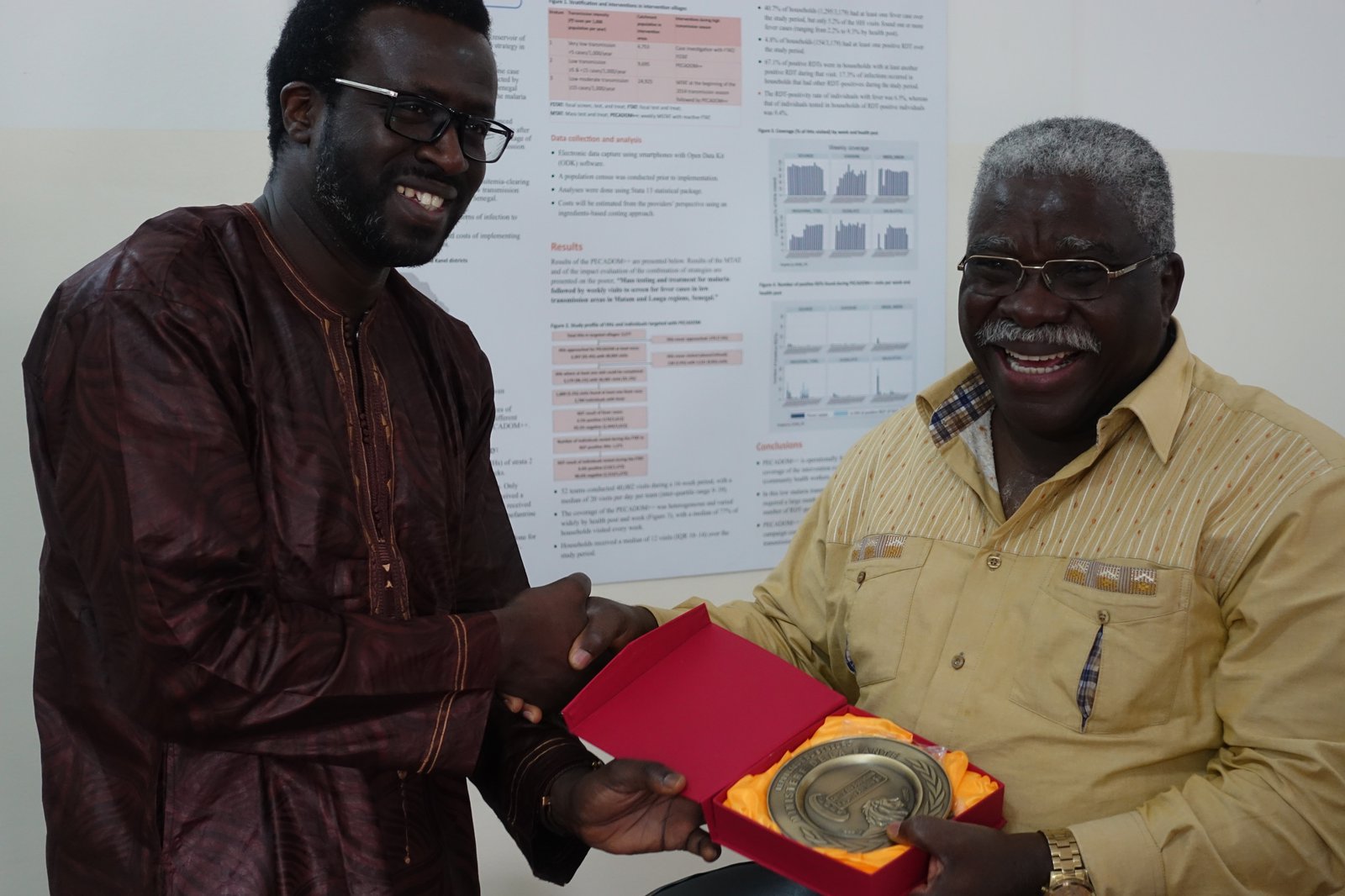 A man presents a gift to another man; both are smiling.