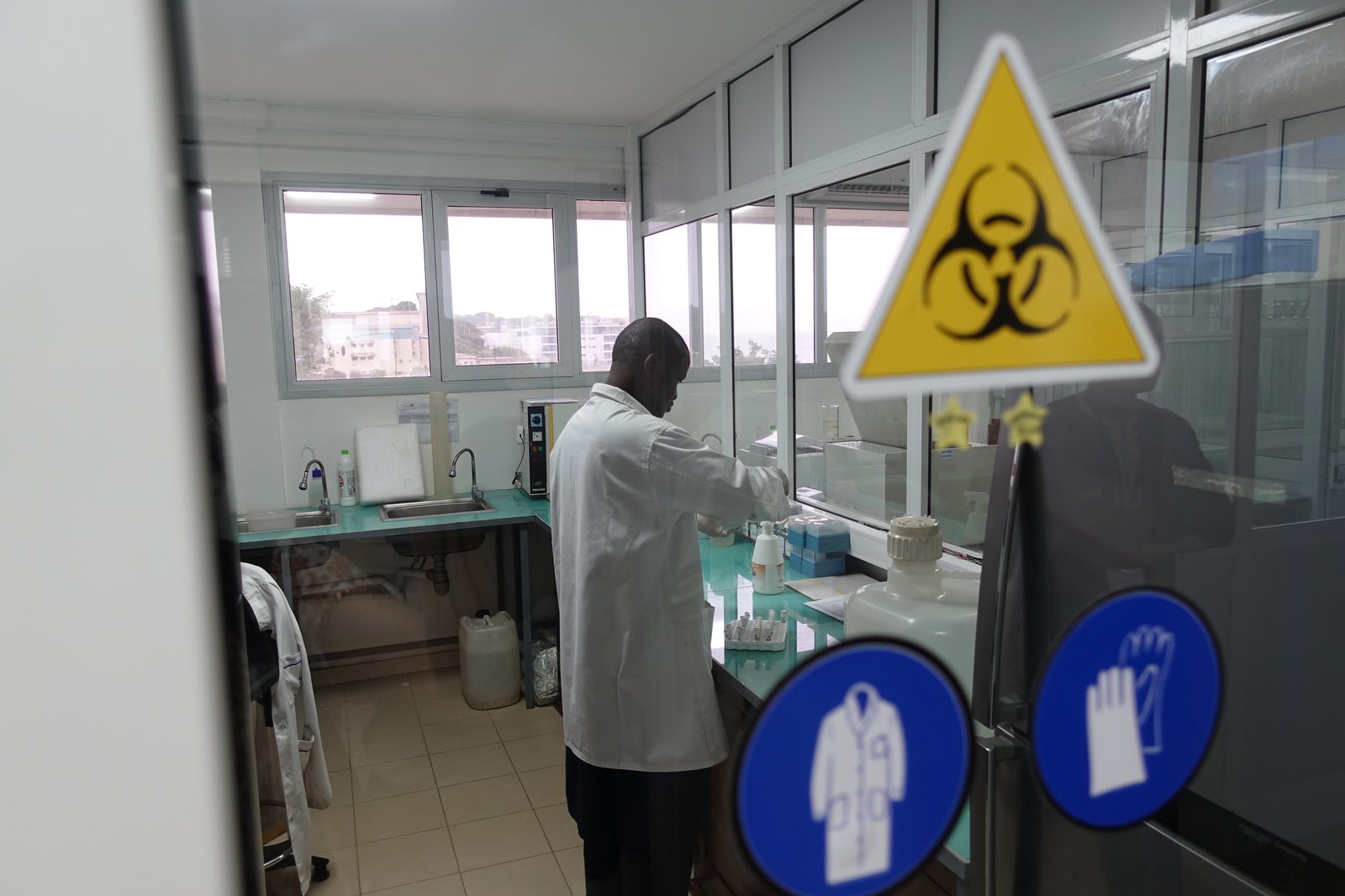 A lab worker in a laboratory facility with a biohazard sign in the foreground. 