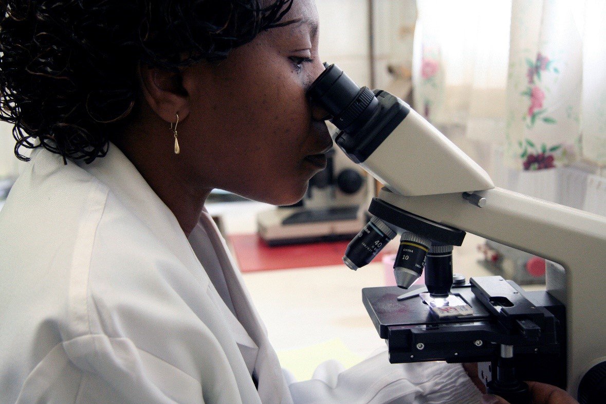 A laboratory worker in Zambia examines a slide under a microscope. Photo: David Jacobs.