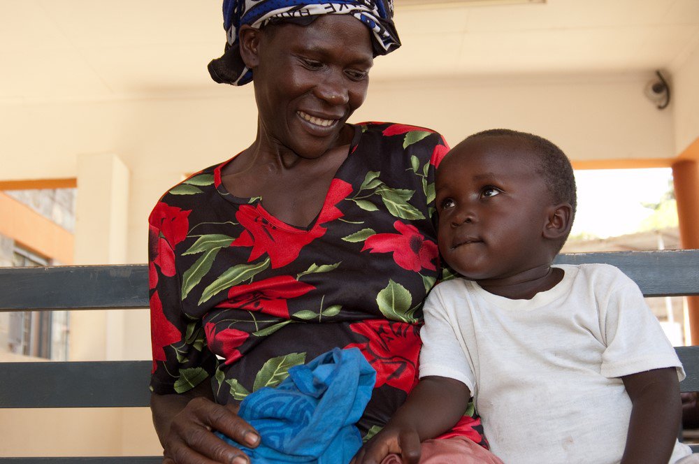 A woman smiles at the toddler son she is sitting next to.