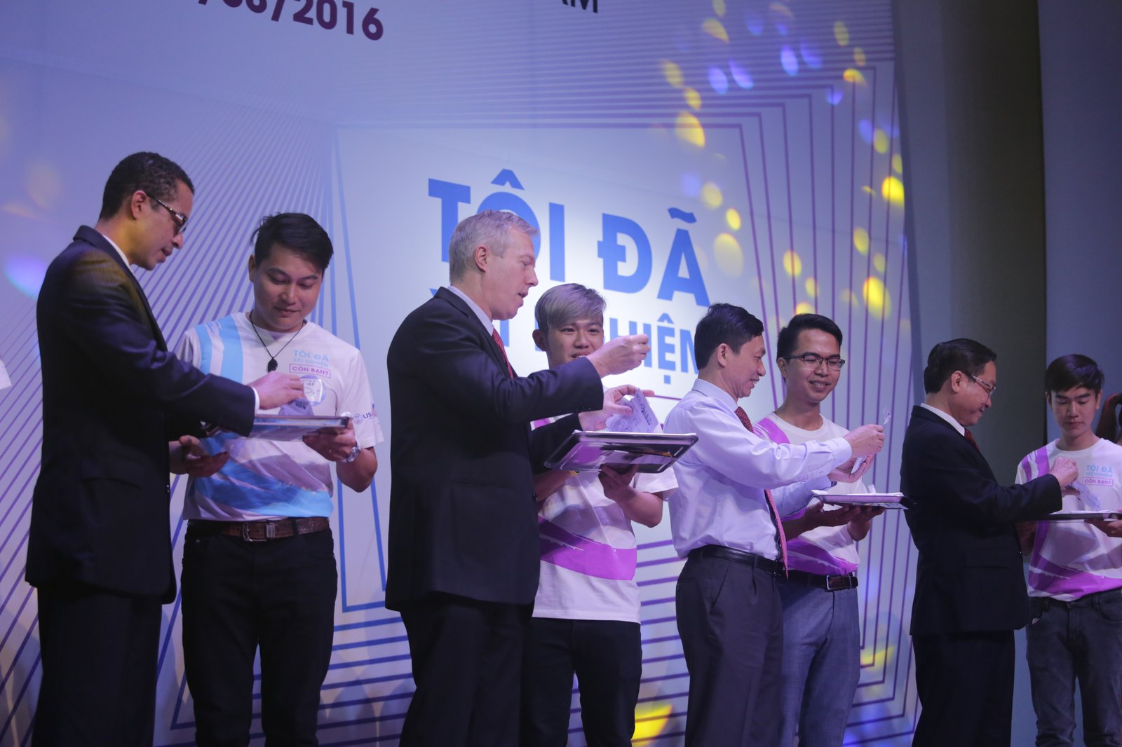 Eight men stand on stage during a celebration. 