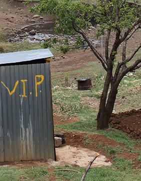 Corrugated steel outhouse with the initials "V.I.P." painted in yellow on the side.