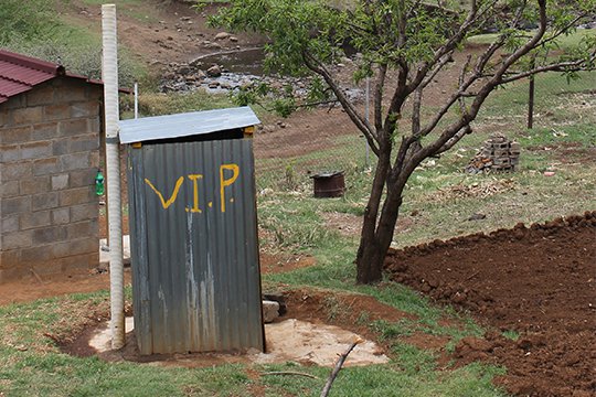 Corrugated steel outhouse with the initials "V.I.P." painted in yellow on the side.