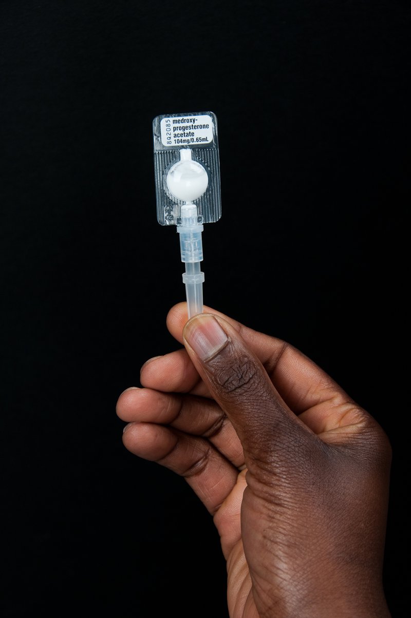 Hand holding injectable contraceptive in device.