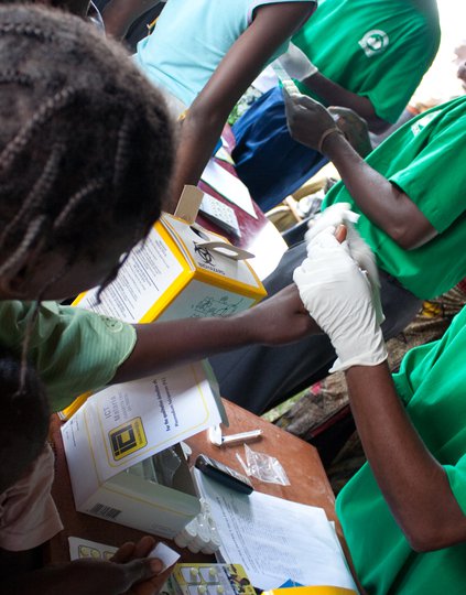 A woman extends her hand, which is held by a health worker who pricks it to draw a drop of blood.