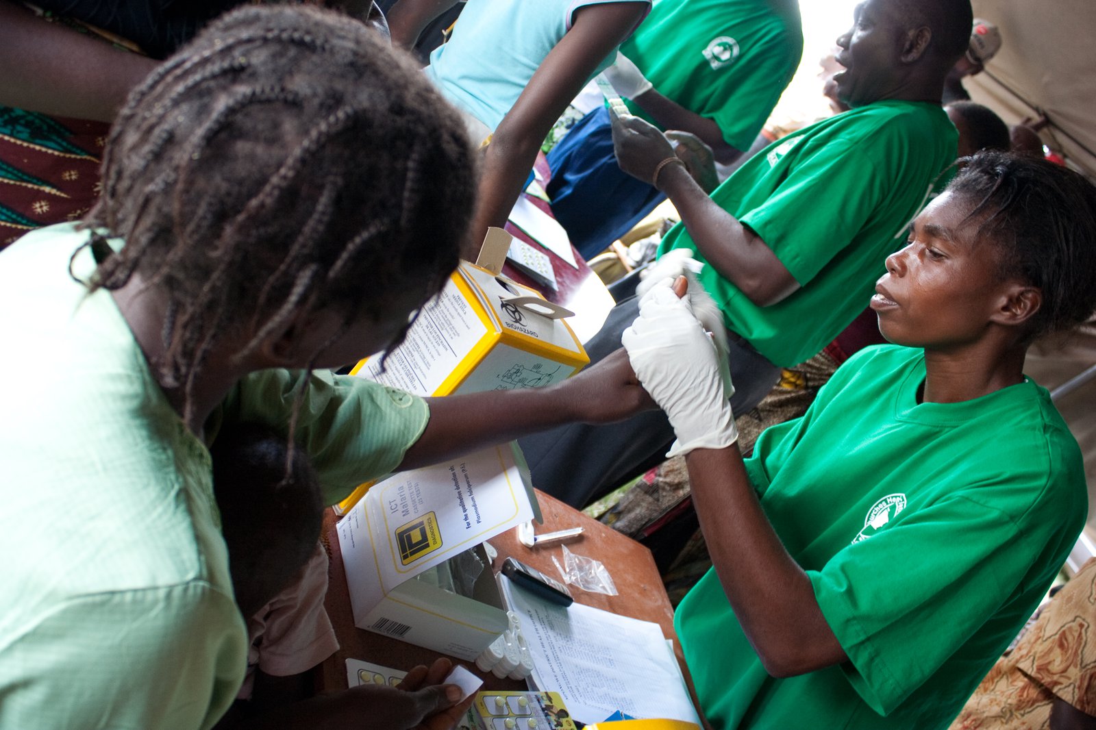 A woman extends her hand, which is held by a health worker who pricks it to draw a drop of blood.