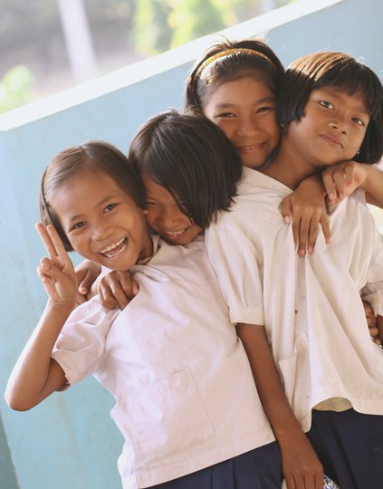 Four giggling young girls in school uniforms pose for the camera.