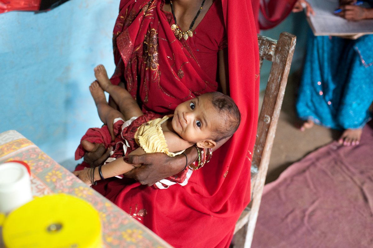 Infant smiles up at camera from her mother's lap.