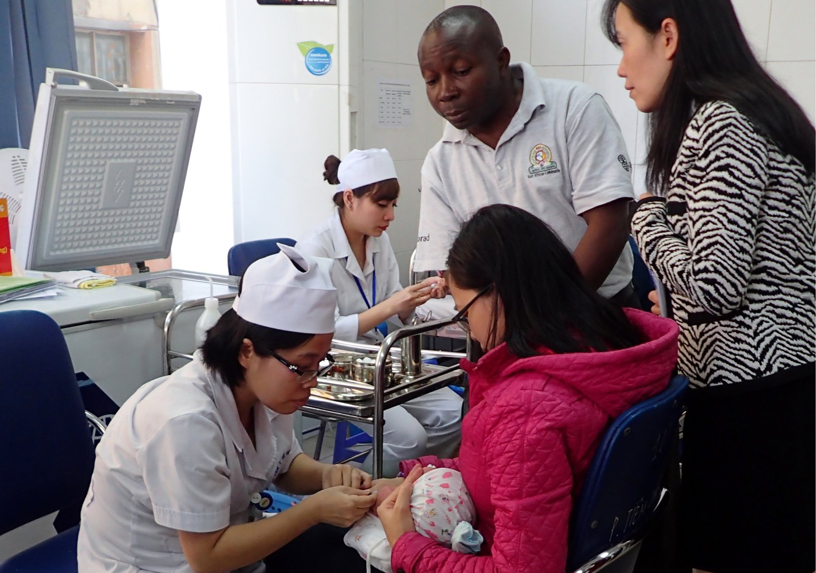 A nurse administers a vaccine to a small child held by a woman as a man looks on.