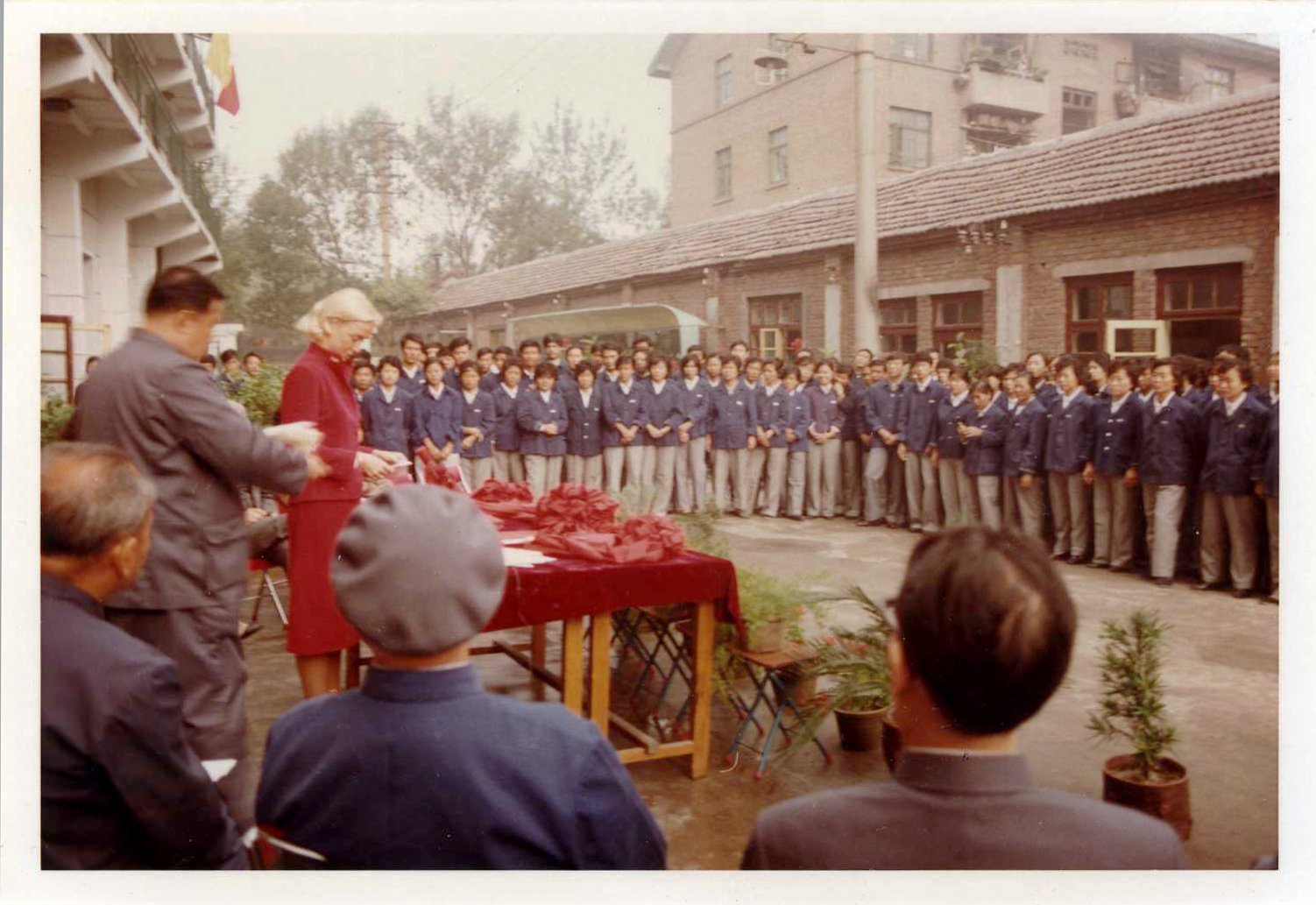 Peggy Morrow, one of PATH's first employees, stands at a podium surrounded by factory workers in China.