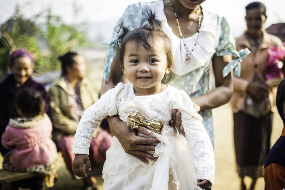 Woman holds a young girl in a fancy white dress. 