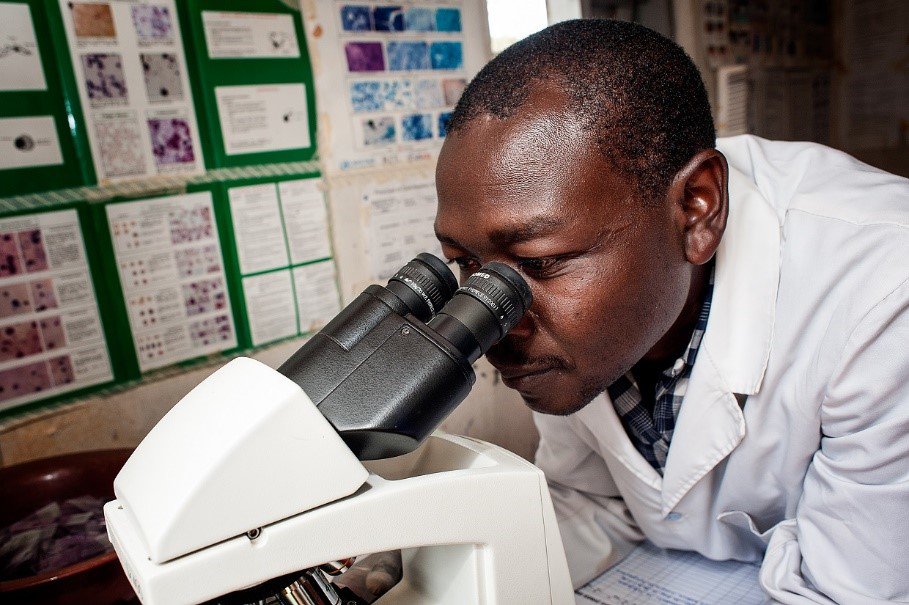 A man wearing a lab coat looks into a telescope.