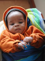 Baby wearing an orange, hooded jacket.