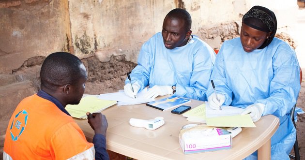 Two health care workers talk to a man across a table. 